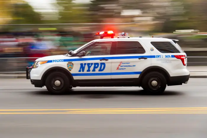 An NYPD vehicle with its lights flashing driving at a high rate of speed against a blurred background.